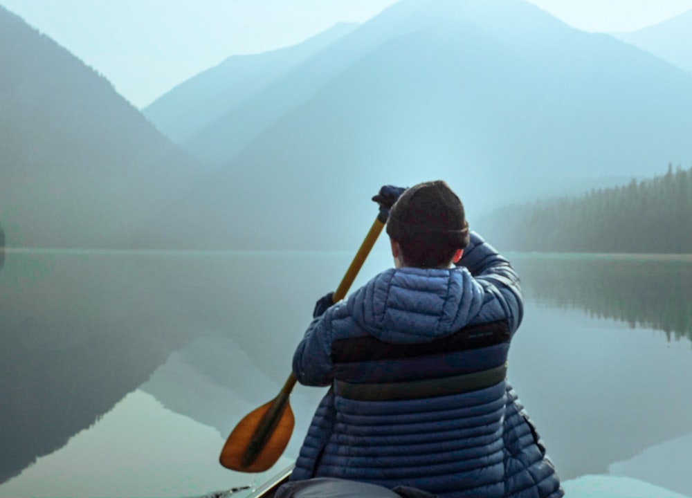 Pagayeur traversant un lac de montagne calme en canot à l'aube